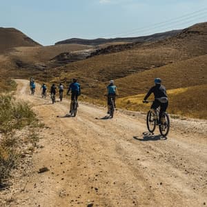 Un viaggio di gruppo WeRoad in mountain bike su una strada sterrata tortuosa attraverso colline aride e marroni sotto un cielo sereno.
