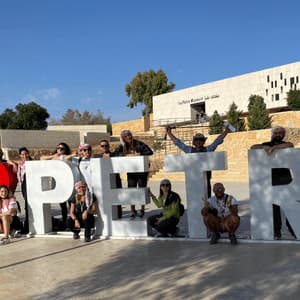 Un gruppo in viaggio WeRoad si mette in posa per una foto attorno alla grande insegna 'I ❤️ PETRA' fuori dal Museo di Petra, sotto un cielo sereno.
