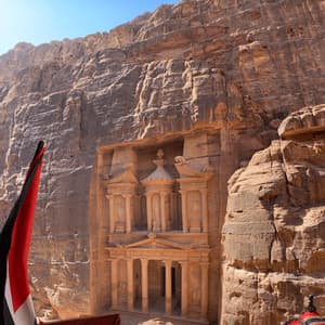 Una facciata ornata scolpita in un'imponente parete rocciosa di arenaria, vista dall'alto con una bandiera e tessuti in primo piano.