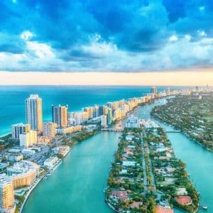 Una veduta aerea di una città costiera con grattacieli lungo l'oceano e isole in un canale turchese sotto un cielo nuvoloso.