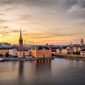 Skyline storico cittadino con campanili lungo il lungomare al tramonto, con una nave bianca ormeggiata a sinistra.
