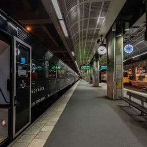 Un treno letto nero con una porta aperta si trova su una banchina vuota e illuminata in una moderna stazione ferroviaria di notte.