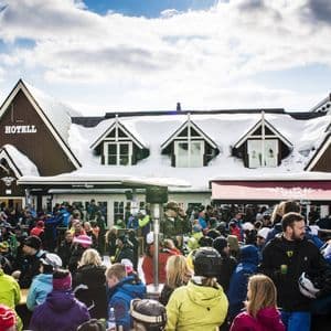 Una grande folla di persone con abiti da sci invernali è radunata fuori da un albergo innevato in una località montana.