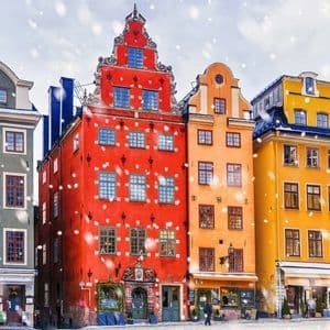 Una fila di edifici colorati e storici in stile europeo che costeggiano una strada acciottolata mentre cade la neve.