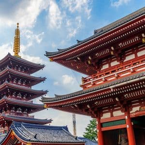 Una pagoda giapponese rossa a più piani e un tradizionale portale del tempio si ergono contro un cielo blu parzialmente nuvoloso.