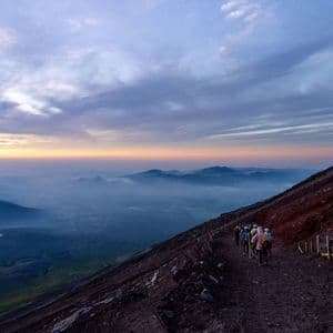 Un gruppo WeRoad in escursione su un ripido sentiero di montagna all'alba, con vista su una vasta e nebbiosa catena montuosa.