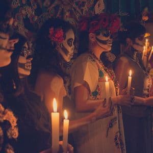 Un viaggio di gruppo WeRoad di donne truccate da Catrina che tengono candele accese durante una celebrazione del Giorno dei Morti.