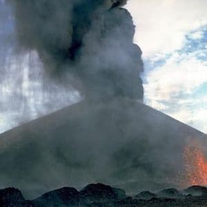 Ein aktiver Vulkan bricht aus und schleudert eine große Säule dunklen Rauchs und Asche in einen bewölkten Himmel, während geschmolzene Lava seine Hänge hinabfließt.