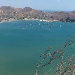 Ein Panoramablick auf eine große blaue Bucht mit vielen Booten, einem Sandstrand und einer Küstenstadt, die sich an trockene Hügel schmiegt.
