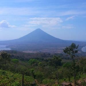Eine malerische Aussicht von einem bewaldeten Hügel auf einen großen Vulkan mit einem See auf der einen und einer Meeresbucht auf der anderen Seite unter blauem Himmel.