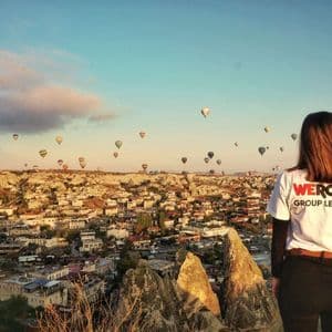 Molte mongolfiere colorate che sorvolano un vasto paesaggio roccioso con formazioni geologiche uniche, sotto un cielo azzurro e limpido.