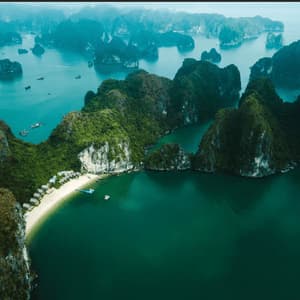 An aerial view of numerous green-topped limestone islands rising from turquoise water, with a secluded sandy beach in the foreground.