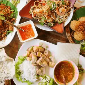 An overhead view of a table spread with various Southeast Asian dishes, including a noodle salad, fried foods, and dipping sauces.