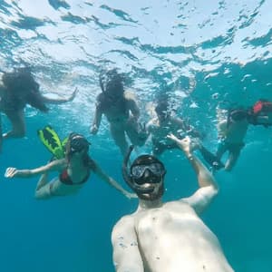 An underwater selfie of a WeRoad group trip snorkeling together in clear blue water, with bubbles rising to the surface.