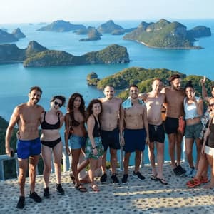 A WeRoad group trip smiles for a photo on a scenic viewpoint overlooking a bay with many green islands.