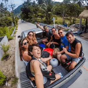 A WeRoad group trip smiles for a selfie while riding together in the open back of a truck on a rural road.