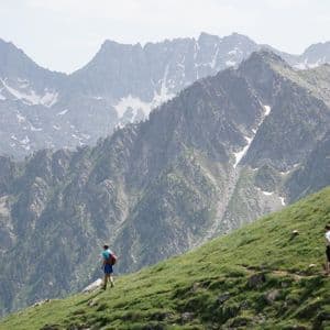 Un grupo de WeRoad de tres personas haciendo senderismo por una ladera de montaña empinada y herbosa, con picos escarpados y nevados de fondo.