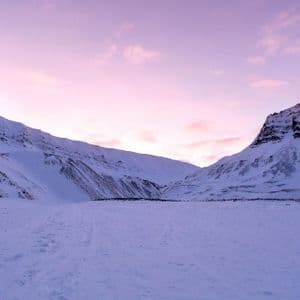 Un vasto valle cubierto de nieve anidado entre montañas bajo un cielo rosa y morado al atardecer.