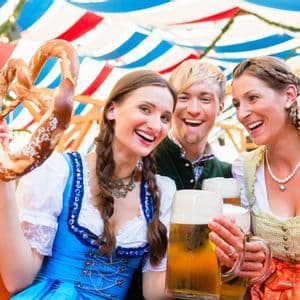 A WeRoad group trip of people in traditional outfits laughing together while holding large beers and pretzels.