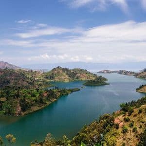 Una vista elevata di un ampio lago blu che serpeggia tra dolci colline coperte di vegetazione verde sotto un cielo parzialmente nuvoloso.