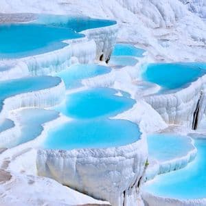 Terraced pools of bright blue water cascade down a white mineral landscape.