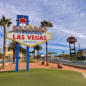 L'iconica insegna 'Welcome to Fabulous Las Vegas' si trova a bordo strada, affiancata da palme sotto un cielo parzialmente nuvoloso.