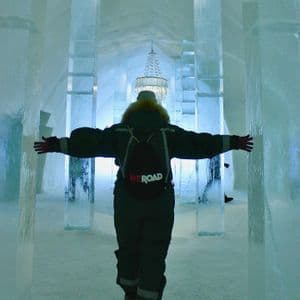 Una persona de espaldas, con una mochila WeRoad, atraviesa un pasillo azul resplandeciente de pilares de hielo, con los brazos extendidos.