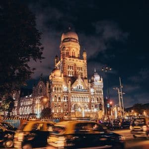 Un grande edificio storico illuminato di notte, con il movimento sfocato dei taxi gialli e neri sulla strada sottostante.