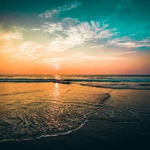 Il sole tramonta sull'oceano, la sua luce si riflette sull'acqua mentre dolci onde bagnano la sabbia umida su una spiaggia.