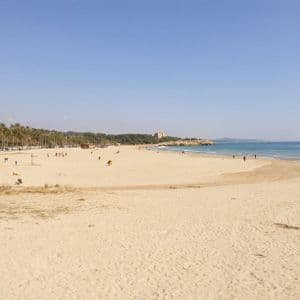 Una spiaggia ampia e sabbiosa con persone sparse lungo la riva, bagnata da acque calme e blu sotto un cielo sereno.