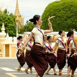 Un grupo de mujeres con atuendos tradicionales de color granate y crema, y joyas de oro, realizan una danza cultural en la calle.
