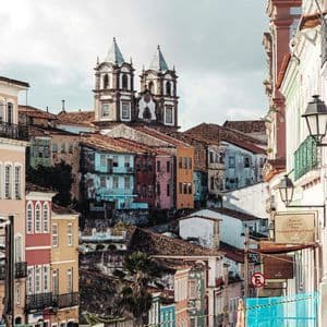 Eine Kopfsteinpflasterstraße führt abwärts durch eine Stadt mit farbenfrohen, historischen Gebäuden und einer im Hintergrund sichtbaren Kirche.