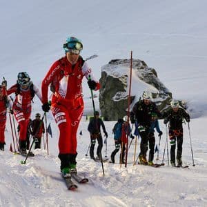 Un gruppo di scialpinisti in tenuta da gara che sale un pendio montano innevato durante una competizione.