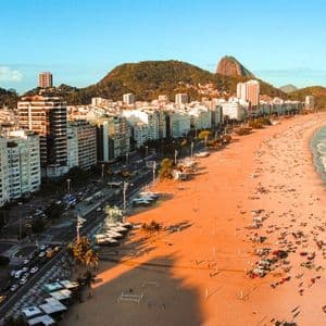 Eine Luftaufnahme eines belebten Stadtstrandes bei Sonnenuntergang, mit Wellen, die an den Sand rollen, und Bergen, die sich hinter den Gebäuden erheben.