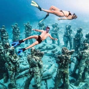 Two people from a WeRoad group trip snorkeling above a circular installation of submerged statues on the seabed.