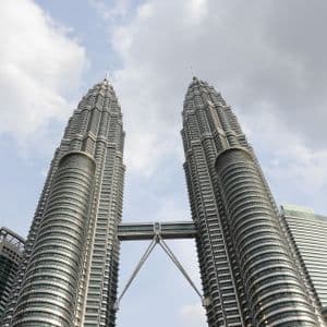 Vista en contrapicado de dos modernos rascacielos con un puente aéreo que los conecta, sobre un cielo azul parcialmente nublado.