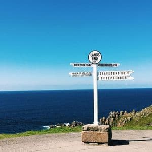 Il cartello bianco di Land's End, che indica le distanze per varie località, affacciato sul mare blu da una scogliera.