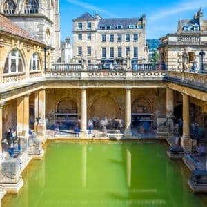 Scatto a lunga esposizione di antiche terme romane con una grande piscina verde, colonnati in pietra e figure sfocate di turisti.