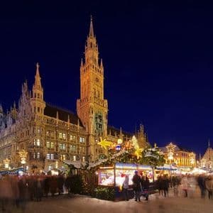 A bustling Christmas market at night, with motion-blurred crowds and festive stalls in front of an illuminated Gothic town hall.