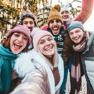 A WeRoad group trip of smiling friends in winter clothes taking a selfie together outdoors with festive lights.