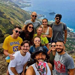 A WeRoad group trip takes a group selfie on a clifftop with a panoramic view of the coastline and ocean below.