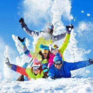 Un viaggio di gruppo WeRoad con abbigliamento da sci colorato che giocano e si lanciano la neve in una giornata di sole circondati da alberi innevati.