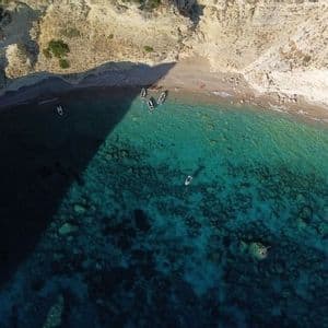 Une vue aérienne d'une crique isolée où de petits bateaux sont amarrés sur la plage et flottent dans la mer turquoise cristalline à côté de falaises abruptes.