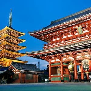 Una tradizionale pagoda giapponese e un grande cancello rosso di un tempio sono illuminati al crepuscolo sotto un cielo blu profondo.