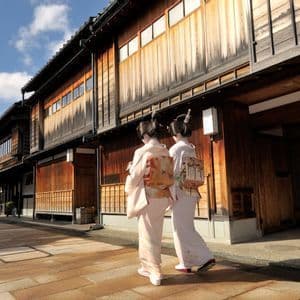 Due donne in kimono tradizionali camminano lungo una strada lastricata fiancheggiata da storici edifici giapponesi in legno.
