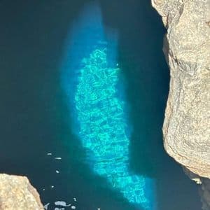 Un parche de agua turquesa vibrante es iluminado por la luz del sol dentro de una piscina natural oscura y rocosa.