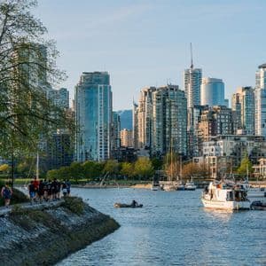 Un gruppo di persone fa jogging lungo un sentiero lungomare, con barche sull'acqua e un fitto skyline della città sullo sfondo.