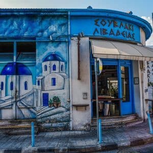 Un negozio all'angolo su una strada cittadina dipinto con un grande murale di edifici bianchi con cupole blu.