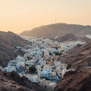 A city of white buildings nestled in a valley between arid, rocky mountains during a golden sunset.