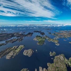 An aerial view of a vast archipelago of rocky, green islands surrounded by deep blue water under a partly cloudy sky.